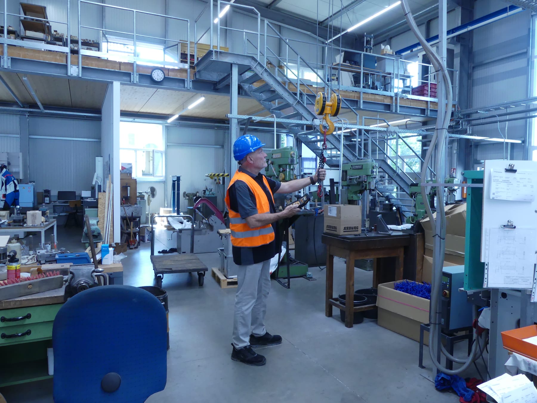 Claus Hauser mit Schutzhelm und Warnweste bei der Prüfung eines Kettenzugs in der Werkstatt